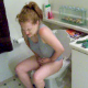 A red-headed woman pees and has a wet-sounding bowel movement while sitting on a toilet. She plays around with her cell phone and does a lot of straining.